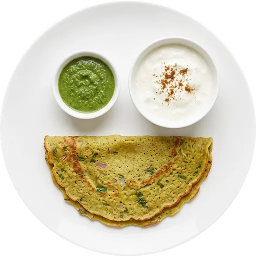 Moong dal chilla with curd and green chutney on a white plate